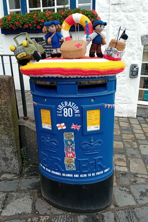 A blue post box with a crocheted toppper